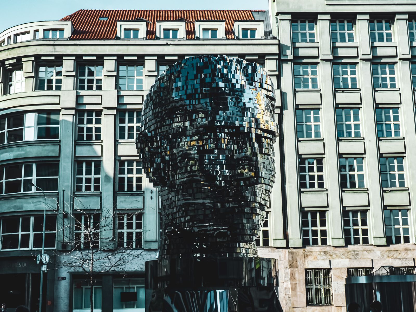 Mirrored Head of Franz Kafka sculpture in front of buildings in Prague