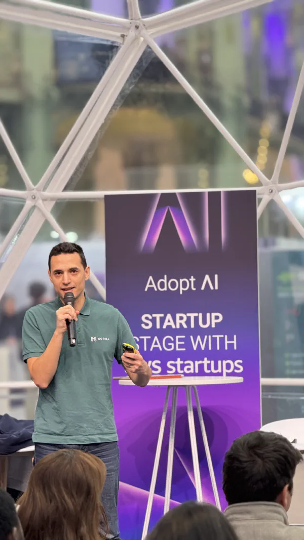 I stand beside the Adopt AI and AWS Startups stage banner